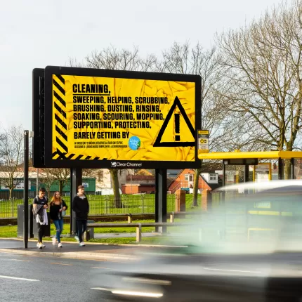 Photo of a campaign billboard at the side of a road with a car driving past