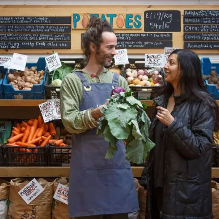 Grocer and client standing in front of grocer stand