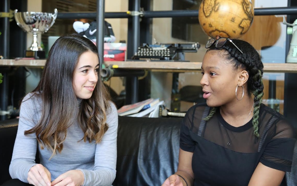 Two women sat down talking in front of some shelves